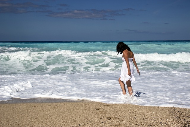 Opálená žena v bielych šatách stojí na kraji mora