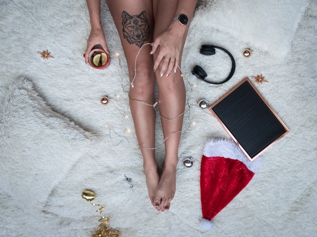 Žena s tetovaním vlka na nohe sedí na posteli s mikulášskou čiapkou.jpg
